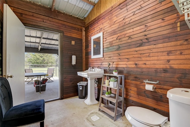 bathroom with toilet, sink, and wood walls