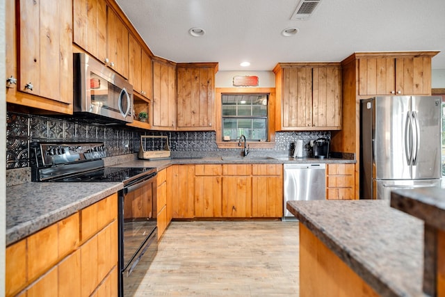 kitchen with stainless steel appliances, tasteful backsplash, sink, and light wood-type flooring