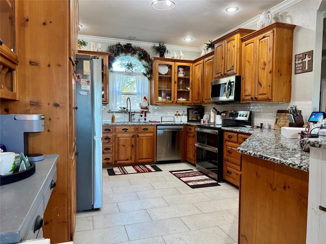 kitchen featuring stainless steel appliances, crown molding, dark stone counters, and sink