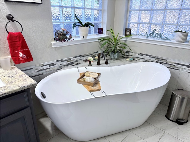 bathroom featuring tile walls, a textured wall, a soaking tub, marble finish floor, and vanity