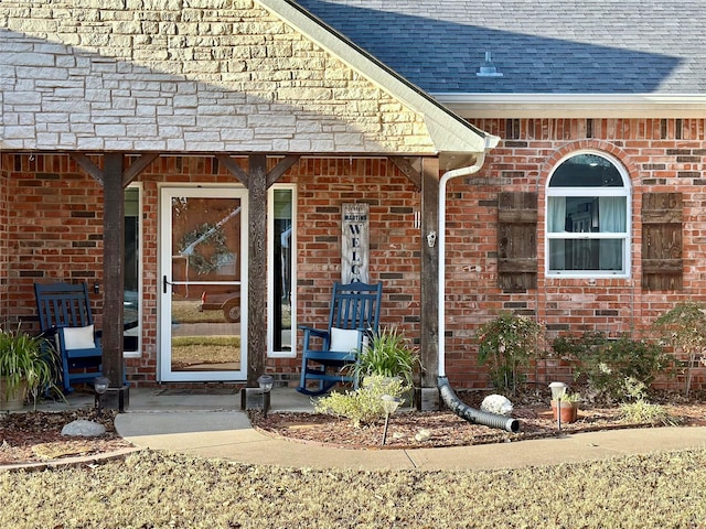 view of exterior entry with brick siding and roof with shingles