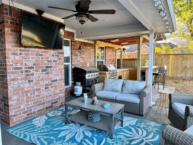 view of patio / terrace featuring fence, exterior kitchen, outdoor lounge area, a grill, and a ceiling fan