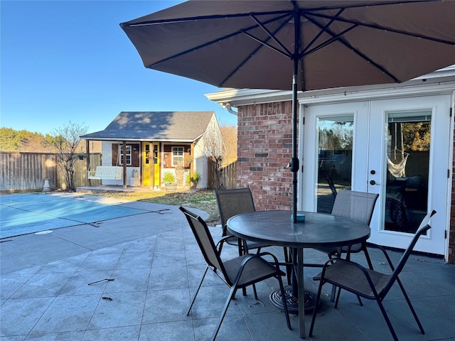 view of patio / terrace featuring outdoor dining space, an outbuilding, fence, and french doors