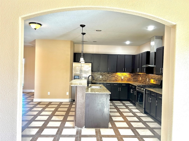 kitchen featuring a kitchen island with sink, light stone countertops, appliances with stainless steel finishes, tasteful backsplash, and decorative light fixtures