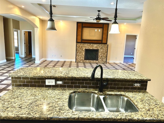 kitchen with a tiled fireplace, ceiling fan, sink, and hanging light fixtures