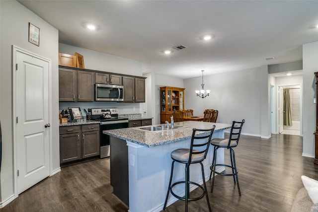 kitchen with dark wood-type flooring, stainless steel appliances, light stone countertops, and a center island with sink