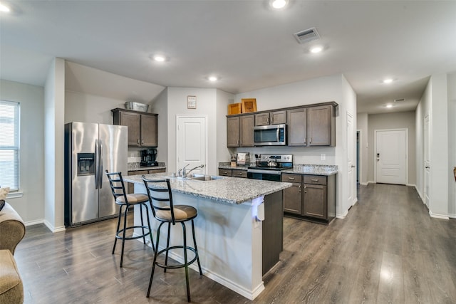 kitchen featuring a breakfast bar, a kitchen island with sink, sink, appliances with stainless steel finishes, and dark hardwood / wood-style flooring