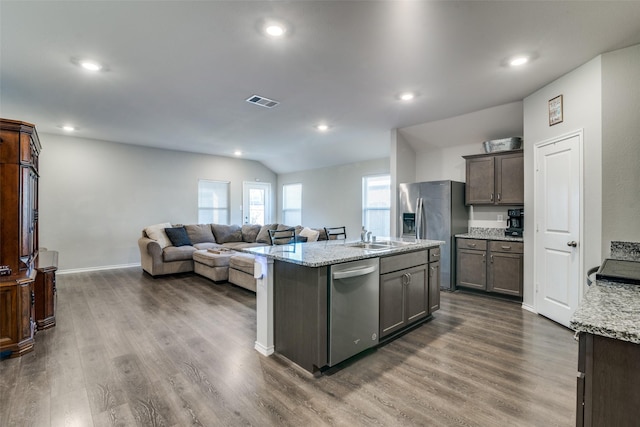 kitchen with dark hardwood / wood-style floors, light stone counters, a kitchen island with sink, and appliances with stainless steel finishes