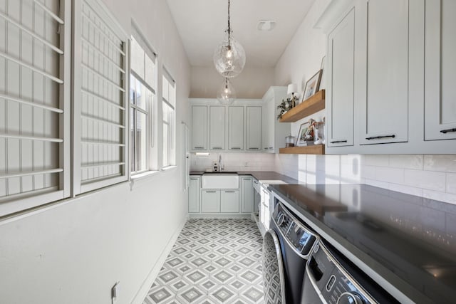 kitchen featuring decorative backsplash, sink, washing machine and clothes dryer, white cabinetry, and hanging light fixtures