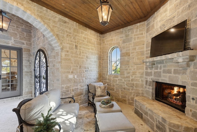 living room with an outdoor stone fireplace and wood ceiling