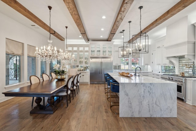 kitchen featuring a large island with sink, beamed ceiling, decorative light fixtures, and premium appliances