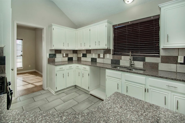 kitchen featuring lofted ceiling, dark stone counters, range, and sink