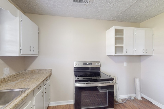 kitchen featuring stainless steel electric range, light wood-type flooring, white cabinetry, and a textured ceiling