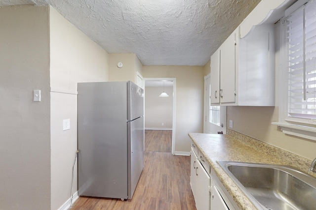 kitchen with white cabinetry, sink, stainless steel fridge, a textured ceiling, and light wood-type flooring