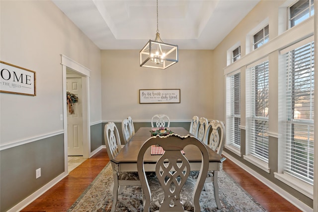 dining space featuring hardwood / wood-style flooring, a raised ceiling, and a notable chandelier