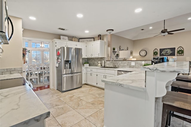 kitchen with light stone countertops, stainless steel appliances, kitchen peninsula, a kitchen bar, and white cabinets