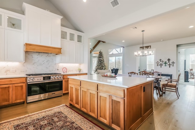 kitchen with a center island, an inviting chandelier, stainless steel range with gas stovetop, white cabinets, and light wood-type flooring