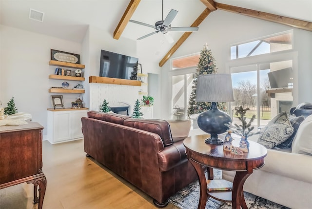 living room featuring beam ceiling, ceiling fan, a brick fireplace, high vaulted ceiling, and light wood-type flooring