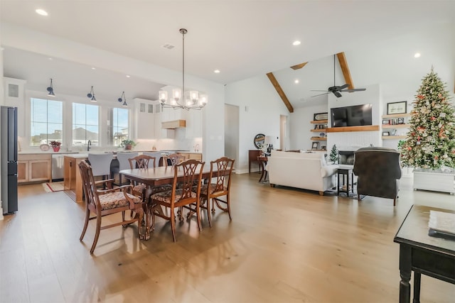 dining room with sink, a brick fireplace, vaulted ceiling with beams, light hardwood / wood-style floors, and ceiling fan with notable chandelier