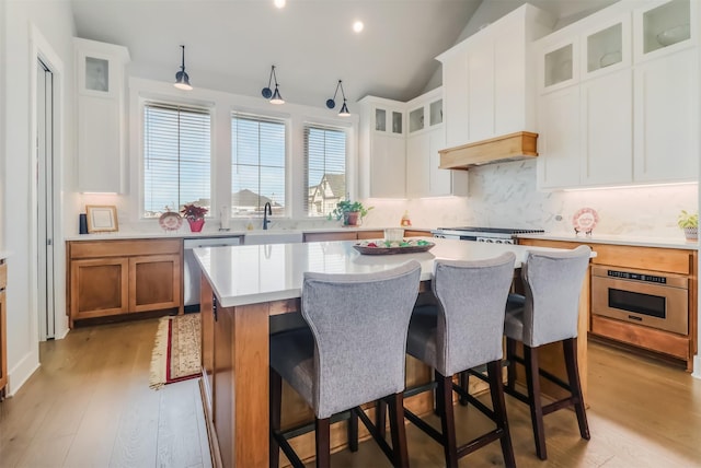 kitchen with custom exhaust hood, a center island, lofted ceiling, light hardwood / wood-style floors, and white cabinetry