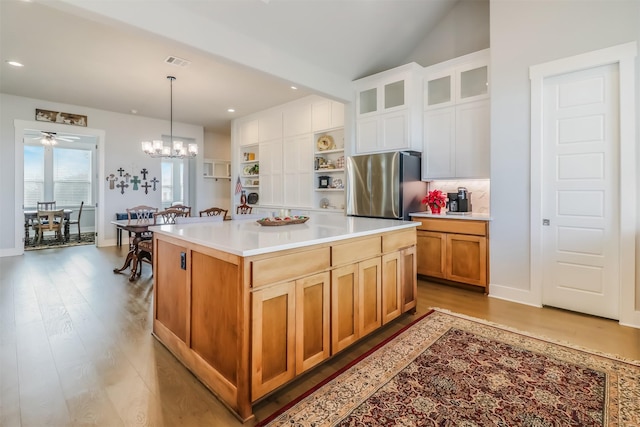 kitchen featuring stainless steel refrigerator, a center island, light hardwood / wood-style flooring, decorative light fixtures, and white cabinets