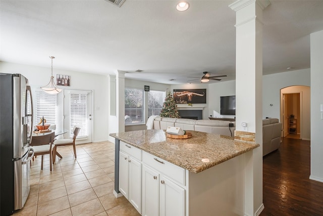 kitchen with pendant lighting, decorative columns, white cabinets, stainless steel fridge, and light stone counters