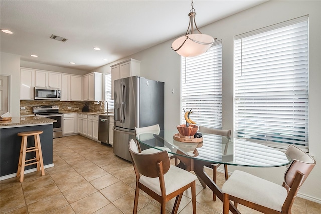 kitchen with tasteful backsplash, white cabinetry, hanging light fixtures, light stone counters, and stainless steel appliances