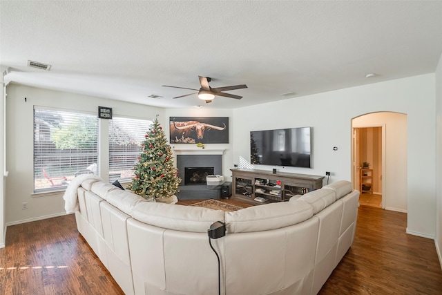 living room with dark wood-type flooring, ceiling fan, and a textured ceiling