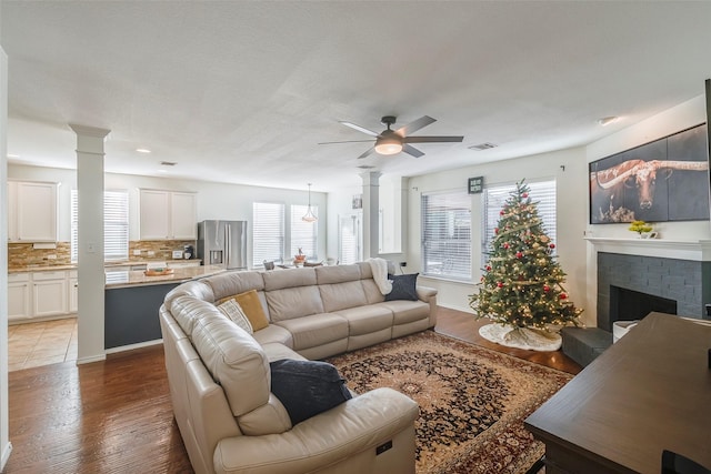 living room with decorative columns, ceiling fan, a brick fireplace, and light hardwood / wood-style floors