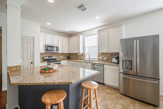 15404 Adlong Dr, Fort Worth, TX 76262 - kitchen featuring appliances with stainless steel finishes, backsplash, a kitchen bar, light stone countertops, and white cabinetry