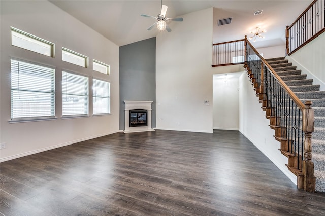 unfurnished living room with ceiling fan, a towering ceiling, and dark wood-type flooring