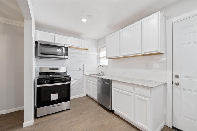 kitchen featuring sink, light stone counters, light hardwood / wood-style flooring, white cabinets, and appliances with stainless steel finishes