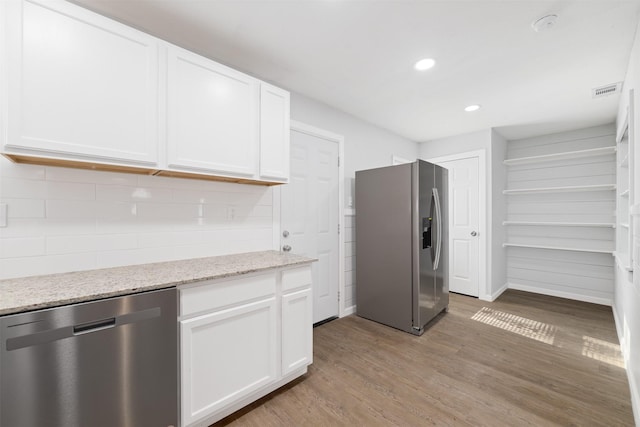 kitchen featuring light stone countertops, light wood-type flooring, tasteful backsplash, stainless steel appliances, and white cabinets