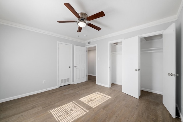 unfurnished bedroom with multiple closets, ceiling fan, hardwood / wood-style floors, and ornamental molding