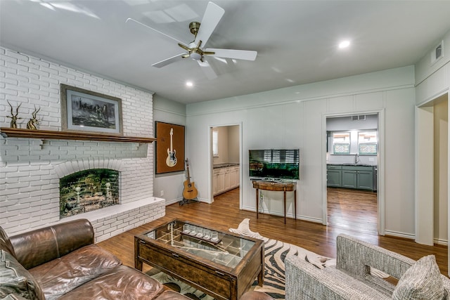 living room with a fireplace, hardwood / wood-style floors, ceiling fan, and sink