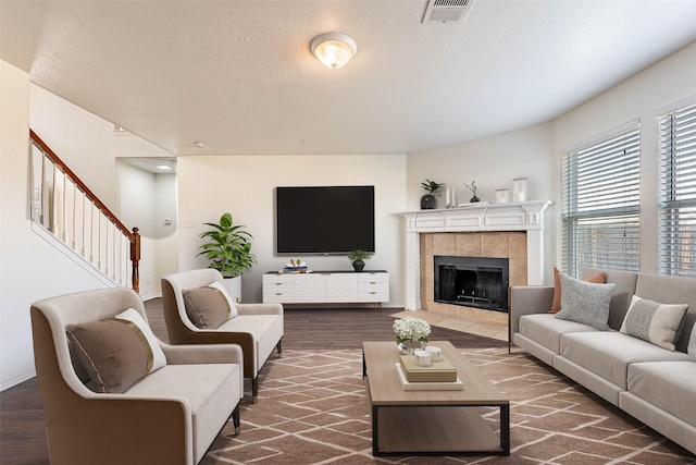 living room with a tile fireplace, a textured ceiling, and dark wood-type flooring