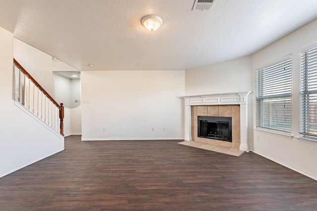 unfurnished living room featuring a tiled fireplace, dark hardwood / wood-style flooring, and a textured ceiling