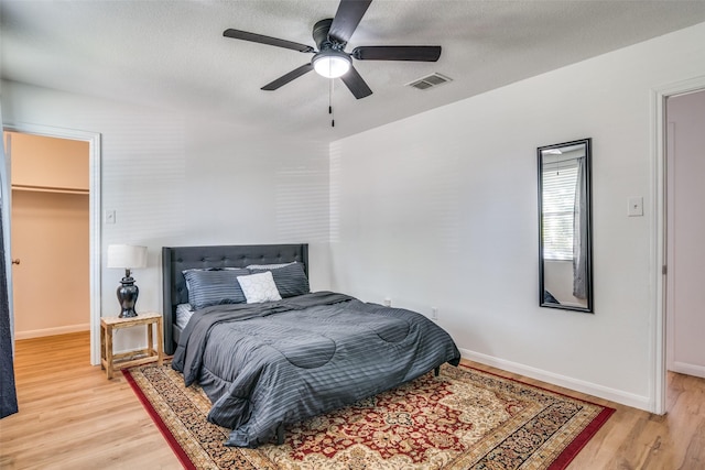 bedroom with a textured ceiling, a spacious closet, light hardwood / wood-style flooring, and ceiling fan