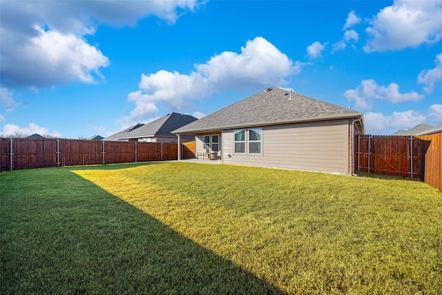 rear view of property with a patio area, a fenced backyard, a shingled roof, and a yard