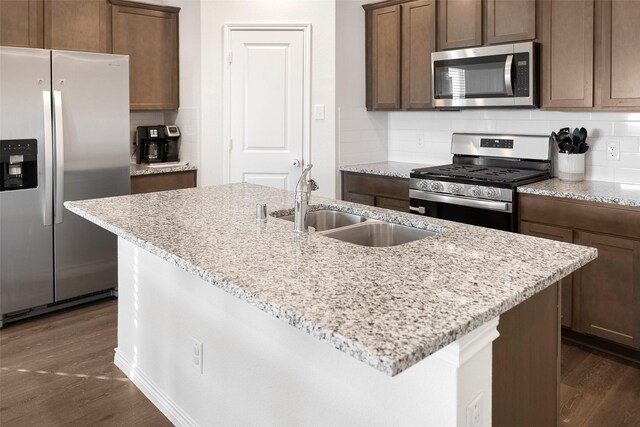 kitchen featuring light stone countertops, sink, dark wood-type flooring, an island with sink, and appliances with stainless steel finishes