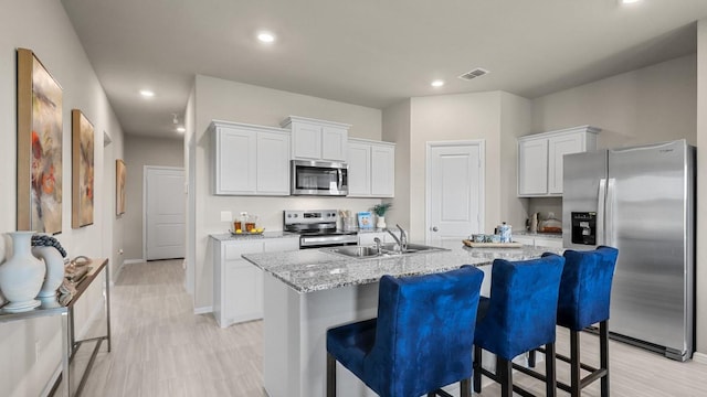 kitchen with a center island with sink, sink, light stone countertops, appliances with stainless steel finishes, and white cabinetry