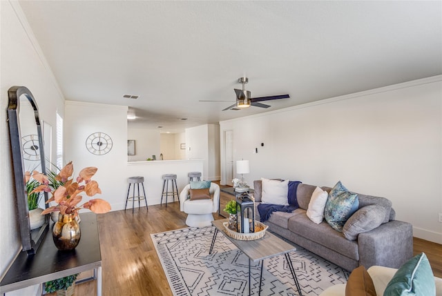 living room featuring a ceiling fan, wood finished floors, visible vents, baseboards, and crown molding