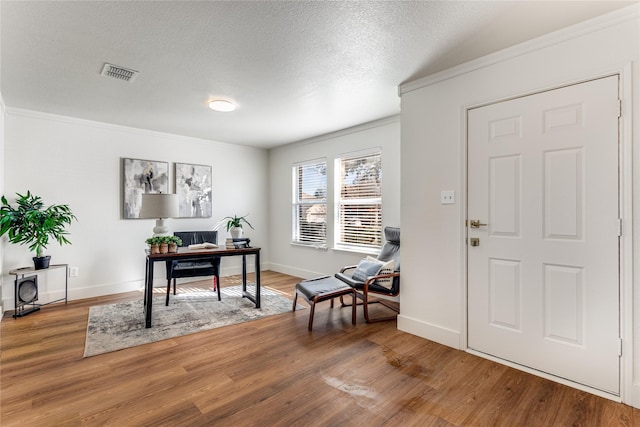 office featuring wood finished floors, baseboards, visible vents, ornamental molding, and a textured ceiling