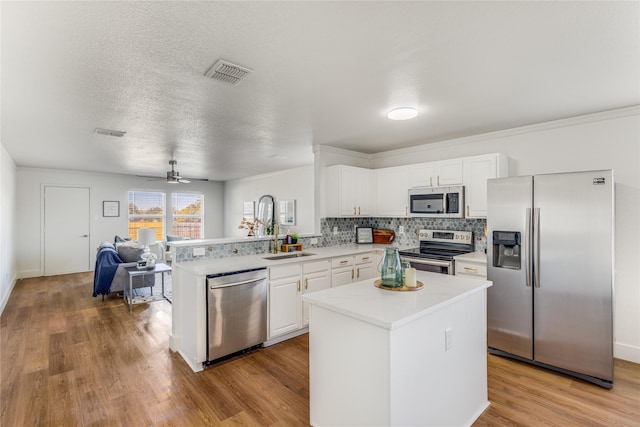 kitchen with visible vents, a peninsula, a sink, light countertops, and appliances with stainless steel finishes