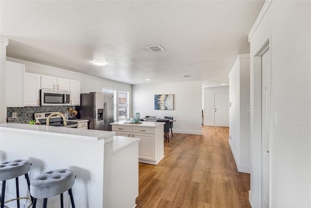 kitchen featuring a kitchen island, a breakfast bar, stainless steel appliances, white cabinetry, and tasteful backsplash