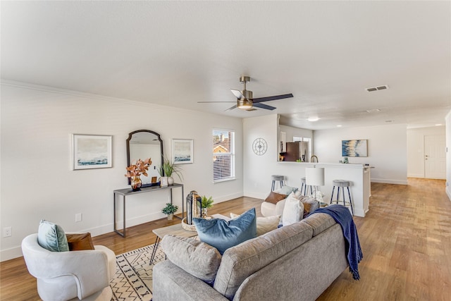 living room with crown molding, light hardwood / wood-style floors, and ceiling fan