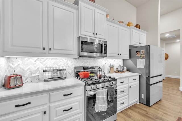 kitchen with tasteful backsplash, light hardwood / wood-style flooring, white cabinets, and appliances with stainless steel finishes