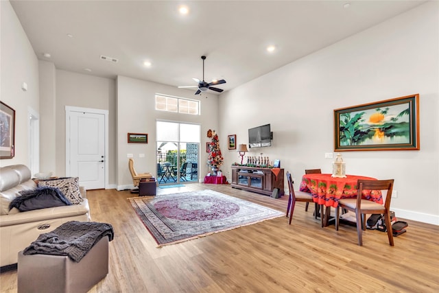 living room with a high ceiling, ceiling fan, and light wood-type flooring