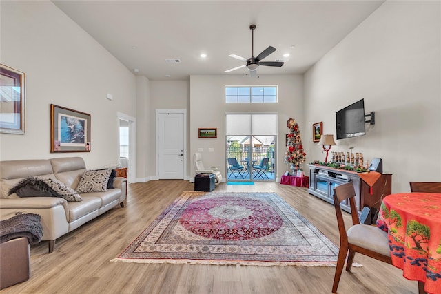 living room with ceiling fan, a towering ceiling, and light hardwood / wood-style floors