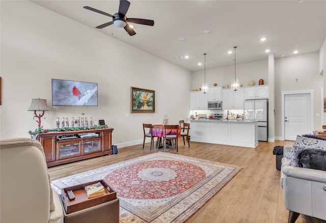 living room with ceiling fan, sink, a high ceiling, and light wood-type flooring